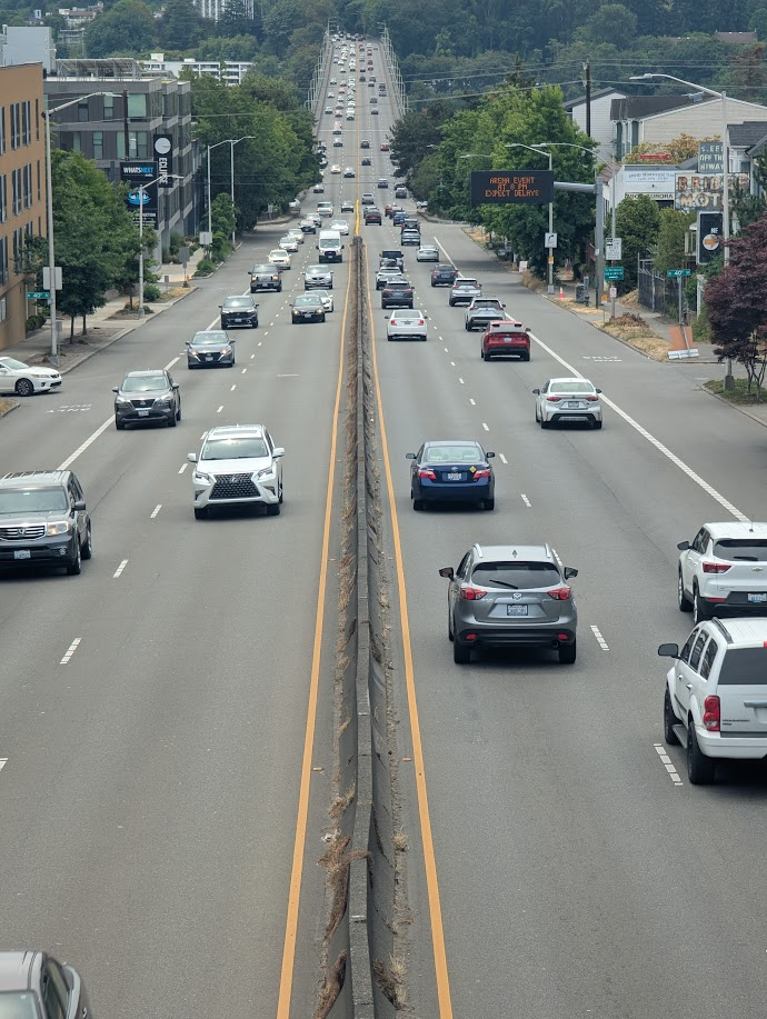 Looking at a 6-lane city street in Seattle filled with cars. Narrow sidewalks and zero visible pedestrians.