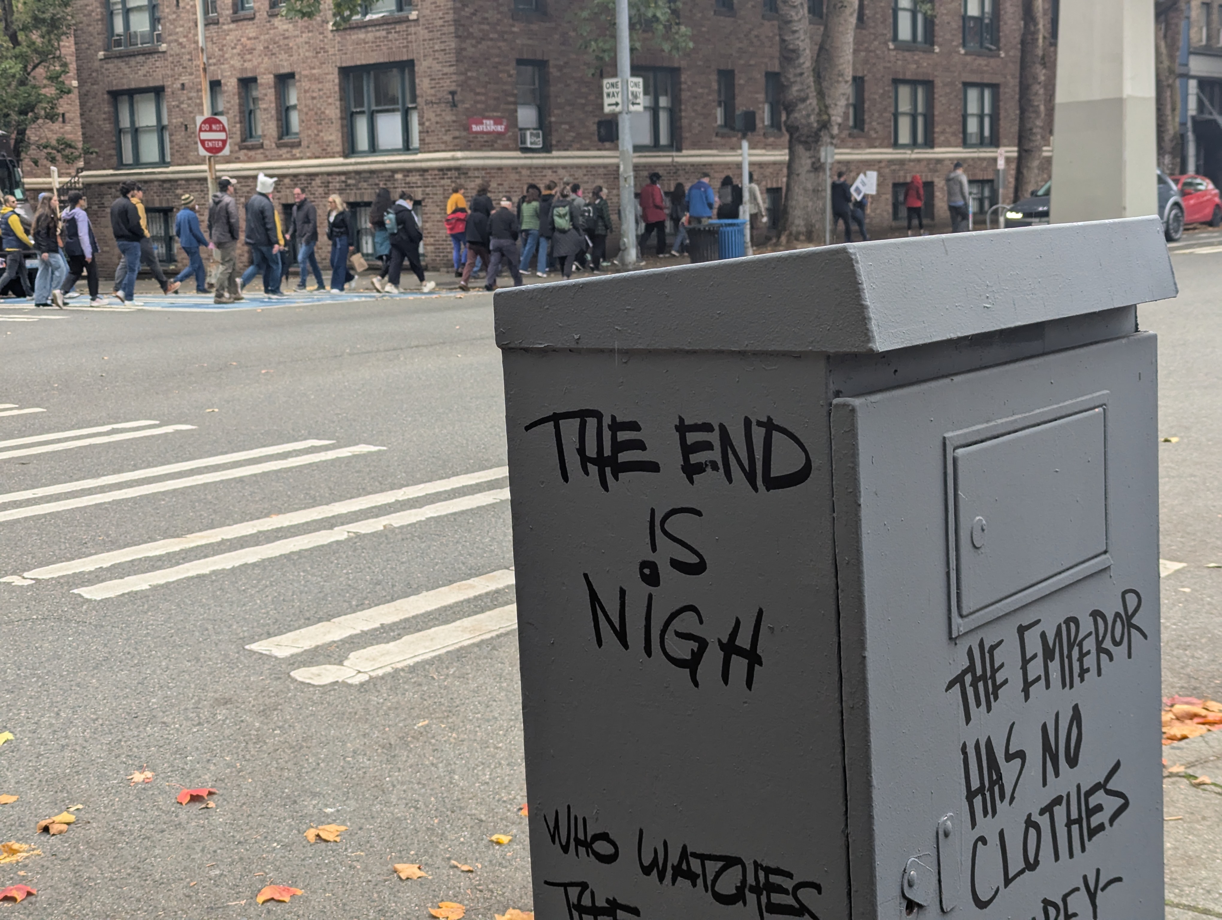 A protest. The foreground includes graffiti that says 'THE END IS NIGH', and 'THE EMPEROR HAS NO CLOTHES'.